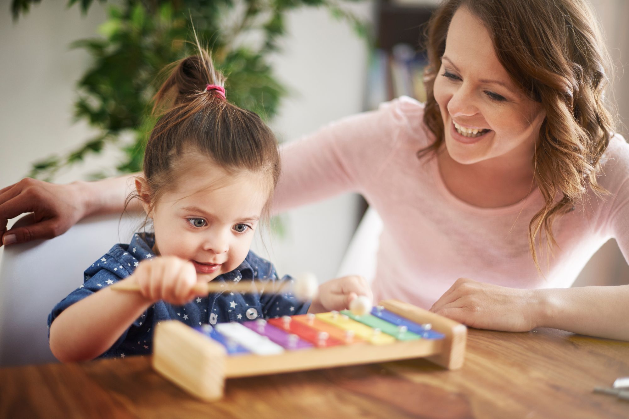 A little girl plays a toy glockenspiel while her mother watches, smiling